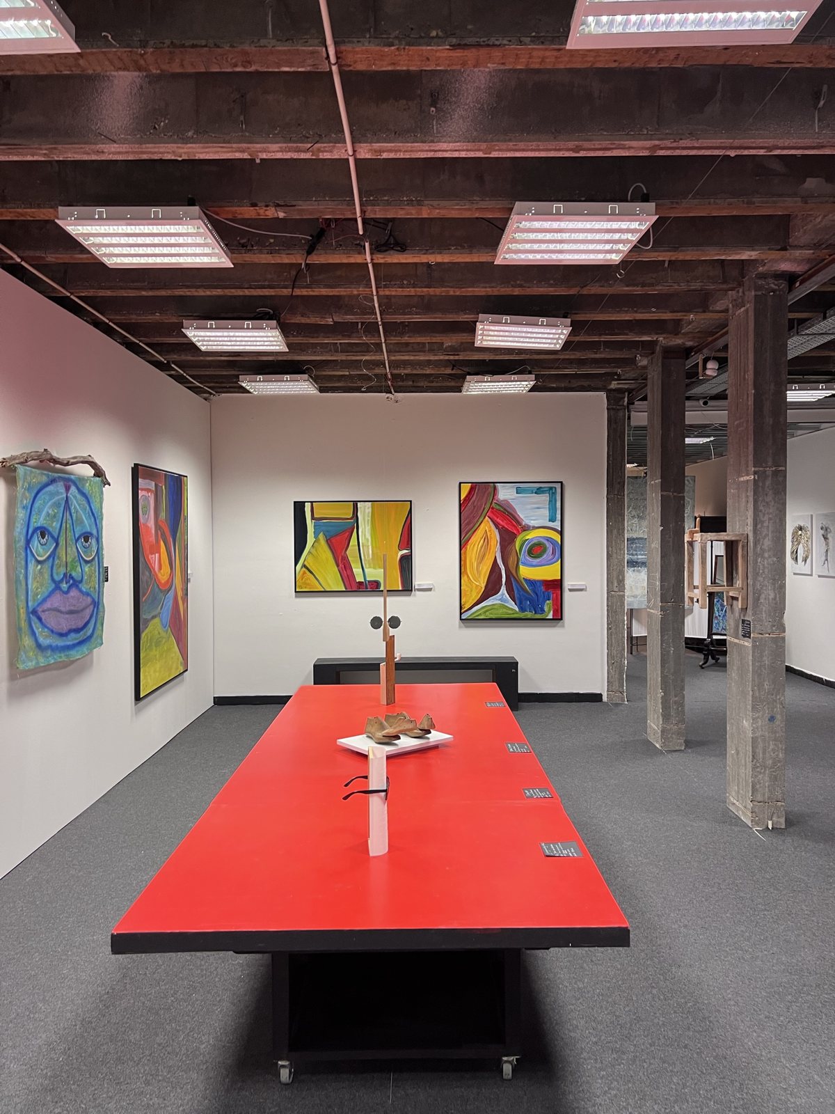 Gallery floor with paintings on white walls and objects on a long red table